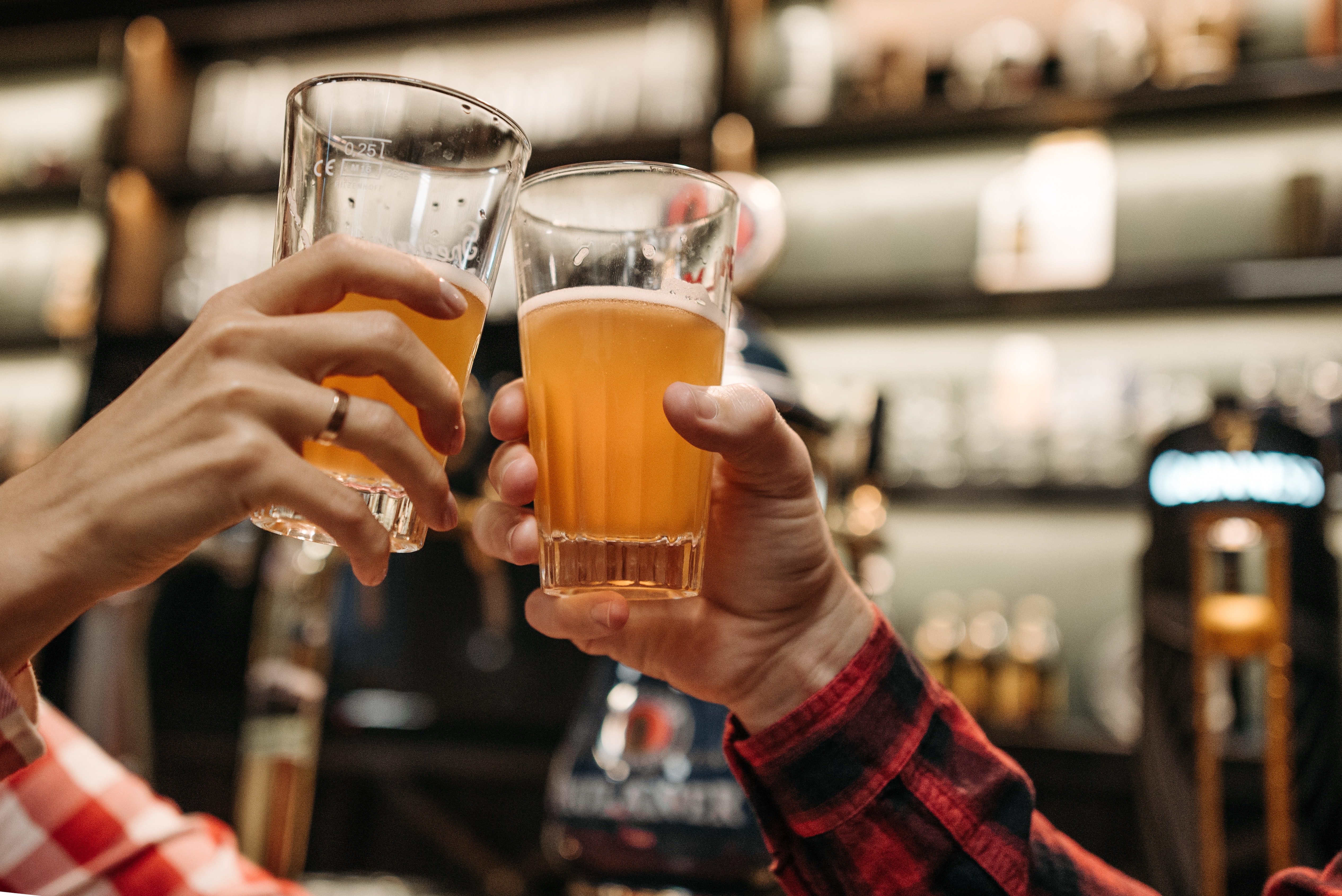 Two hands holding pints of beer. They are clinking glasses as if to say "Cheers."