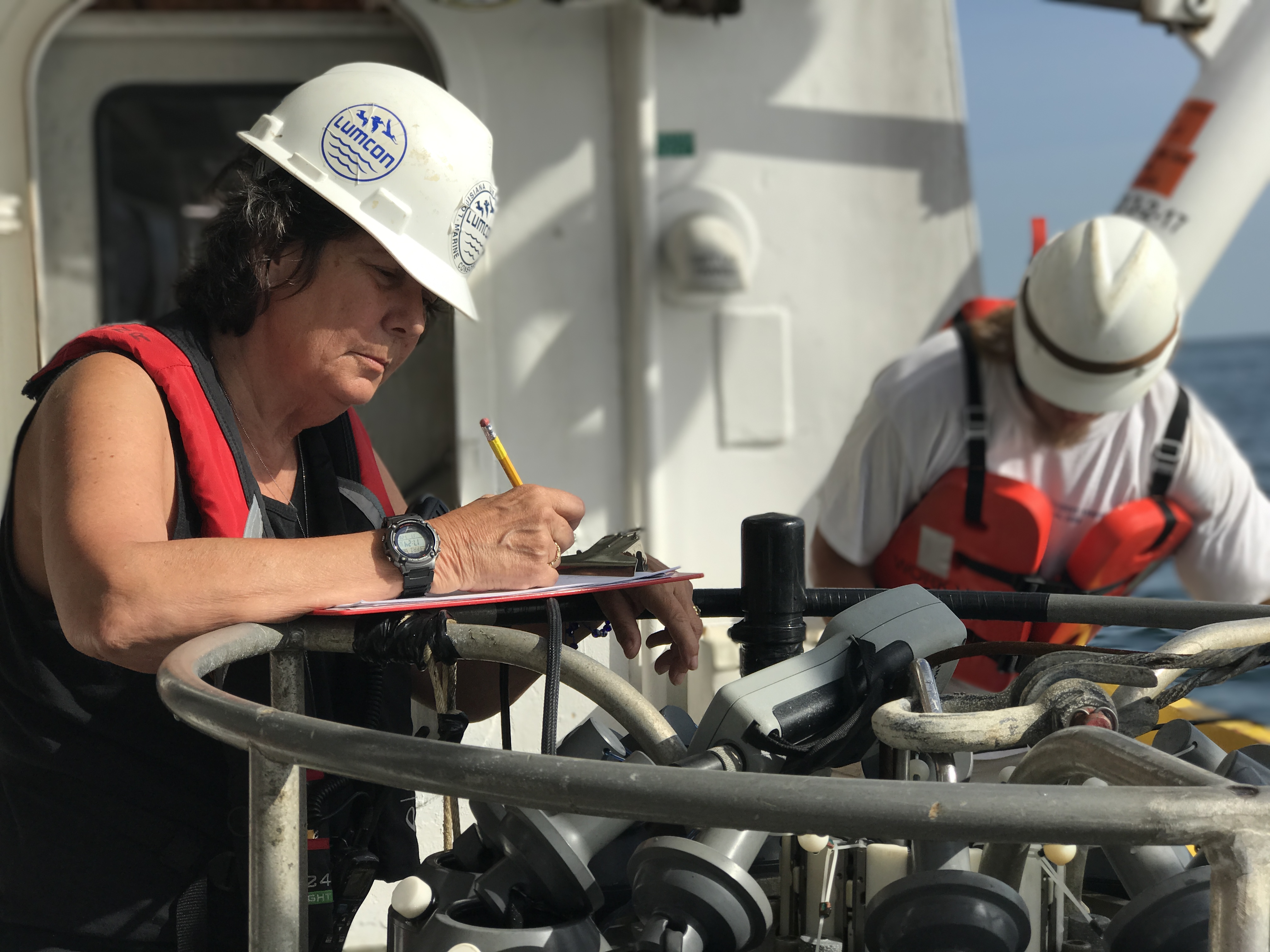 Nancy Rablais and a colleague, both wearing a white protective hard hat, doing work on a boat.