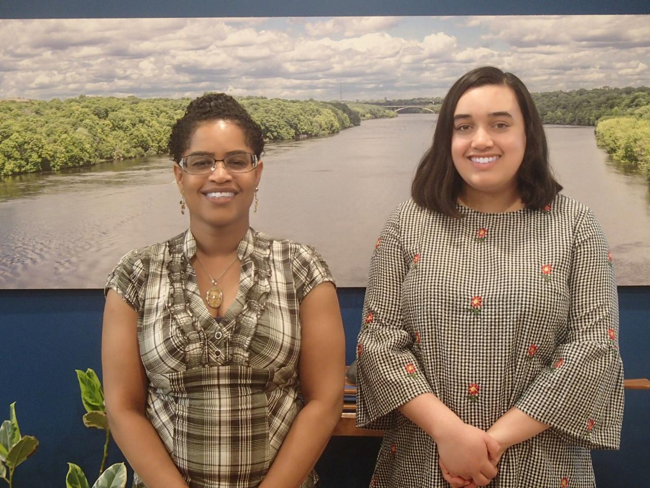 Raynette Prince and Sophie Downey stand before a large photo of the Mighty Mississippi.