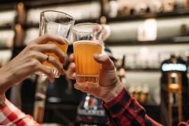 Two hands are holding half-full beer glasses. The glasses are being clinked.