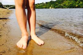 Bare feet standing on the sand along the shores of the Mississippi River in the Twin Cities.