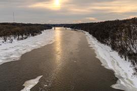 Snowy icy river with bare trees on riverbanks