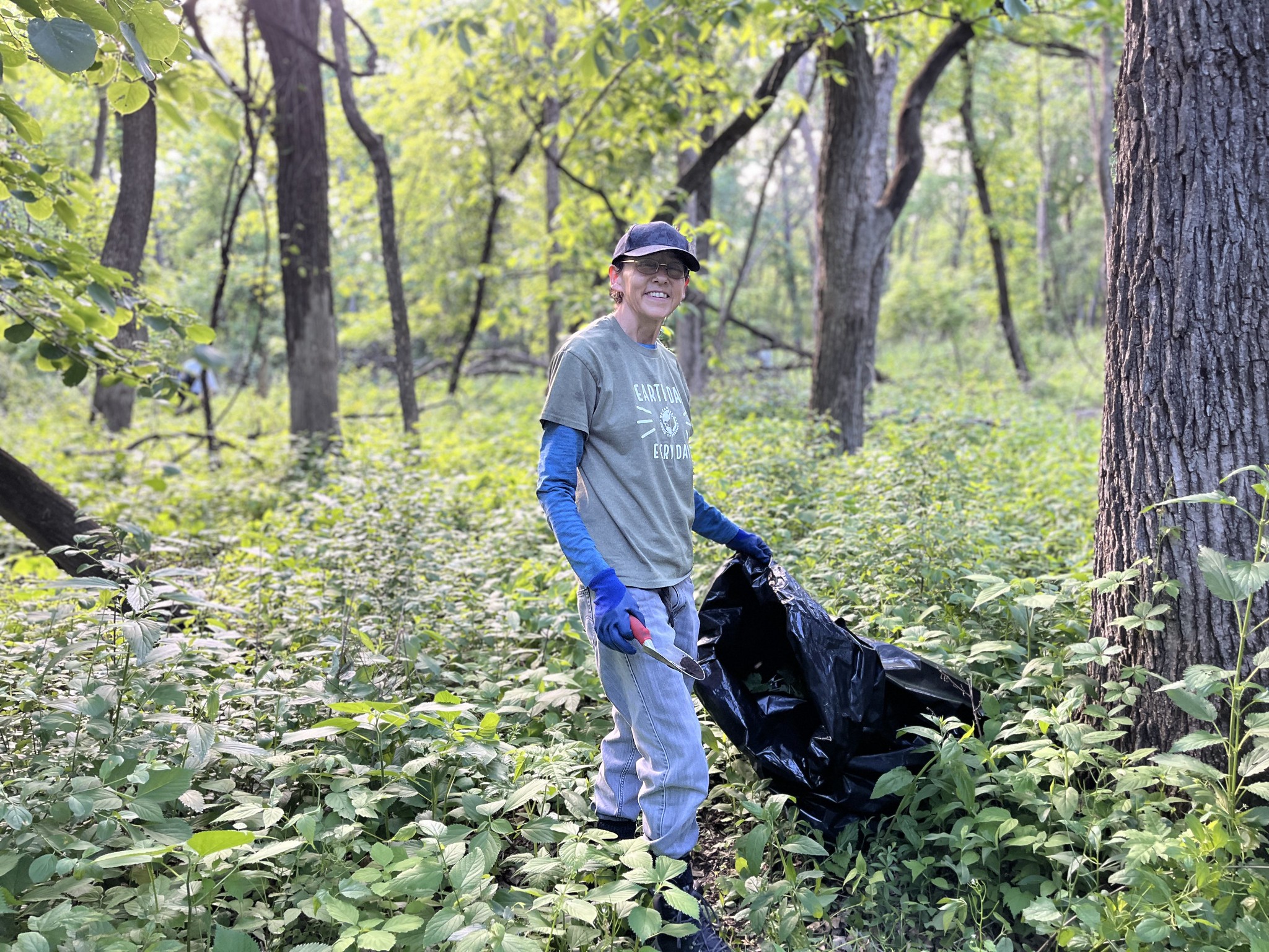 A volunteer holds a black trash bag in a forest