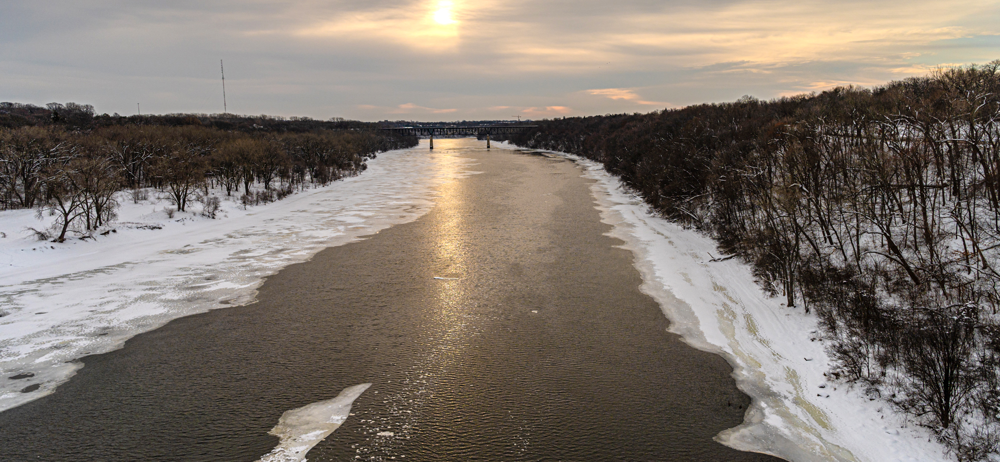 Snowy icy river with bare trees on riverbanks